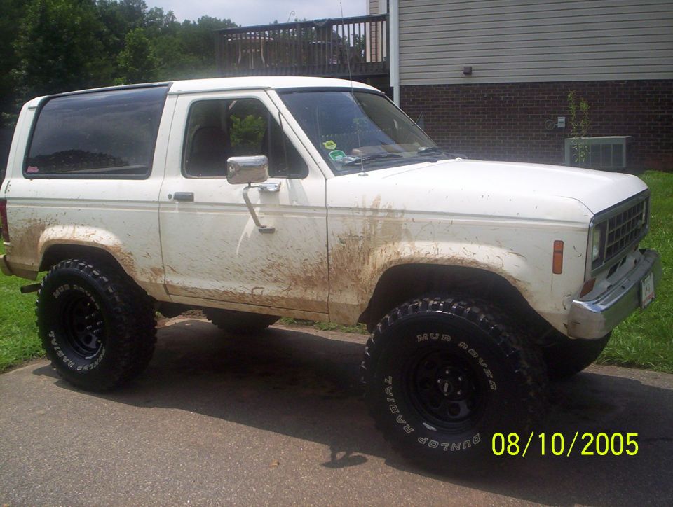 Mud-splattered white Ford Bronco II on Dunlop Mud Rover tires, passenger-side view