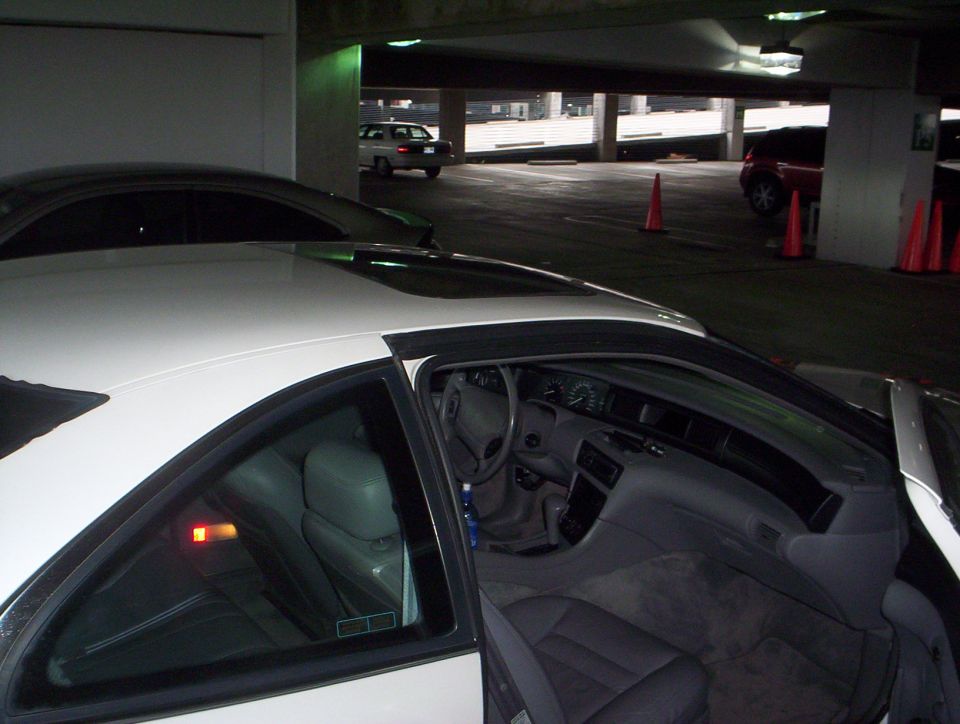 White coupe with driver door open showing gray leather interior in a parking garage
