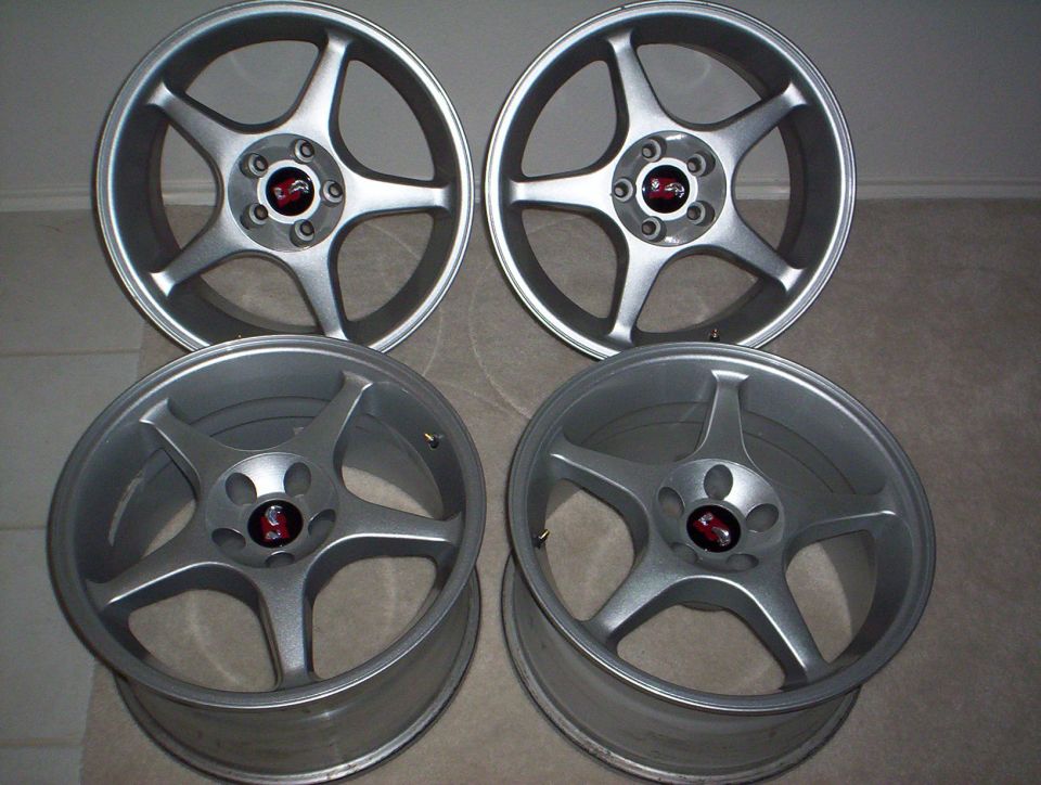 Set of four silver five-spoke alloy wheels with red center caps on a floor