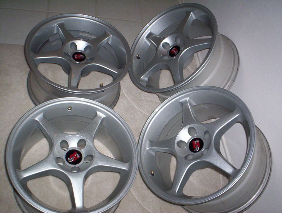 Four silver five-spoke alloy wheels with red center caps on a tile floor