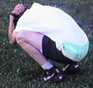 1984 Ford Bronco II - A person is seen crouching down on a grassy area, with their head covered by a white shirt.