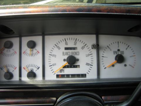1990 Ford Bronco - vehicle gauge cluster with side gauges, a tachometer and a central speedometer face labeled BLANCO BRONCO over the odometer.