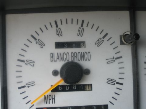 1990 Ford Bronco - Close-up of a white speedometer dial reading MPH with an orange needle, the words BLANCO BRONCO printed above the odometer.