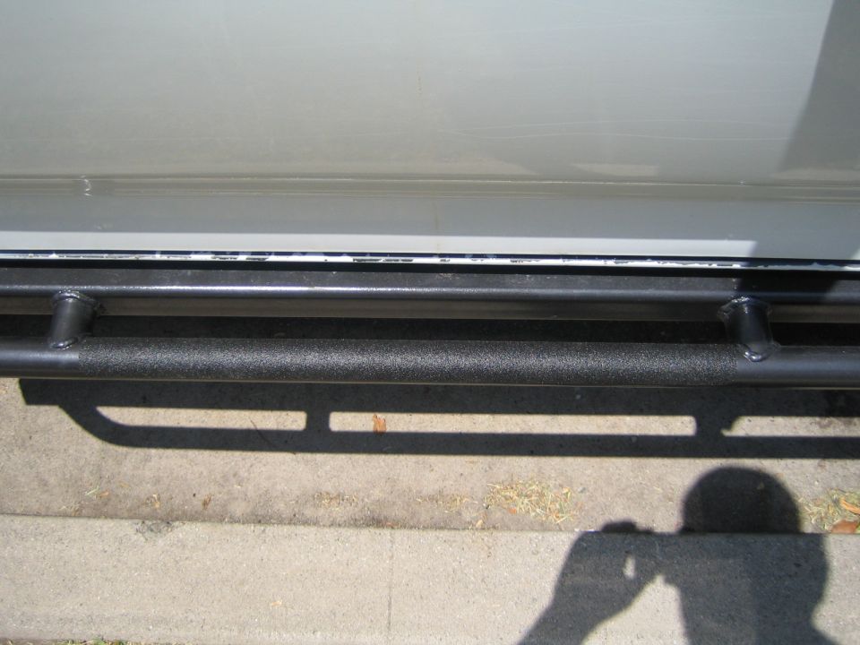 Black textured-coated tubular rock-slider step bar under the rocker of a vehicle