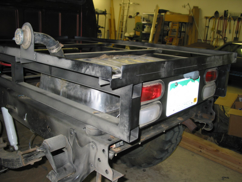 Black steel flatbed frame with taillights mounted on a vehicle chassis in a workshop