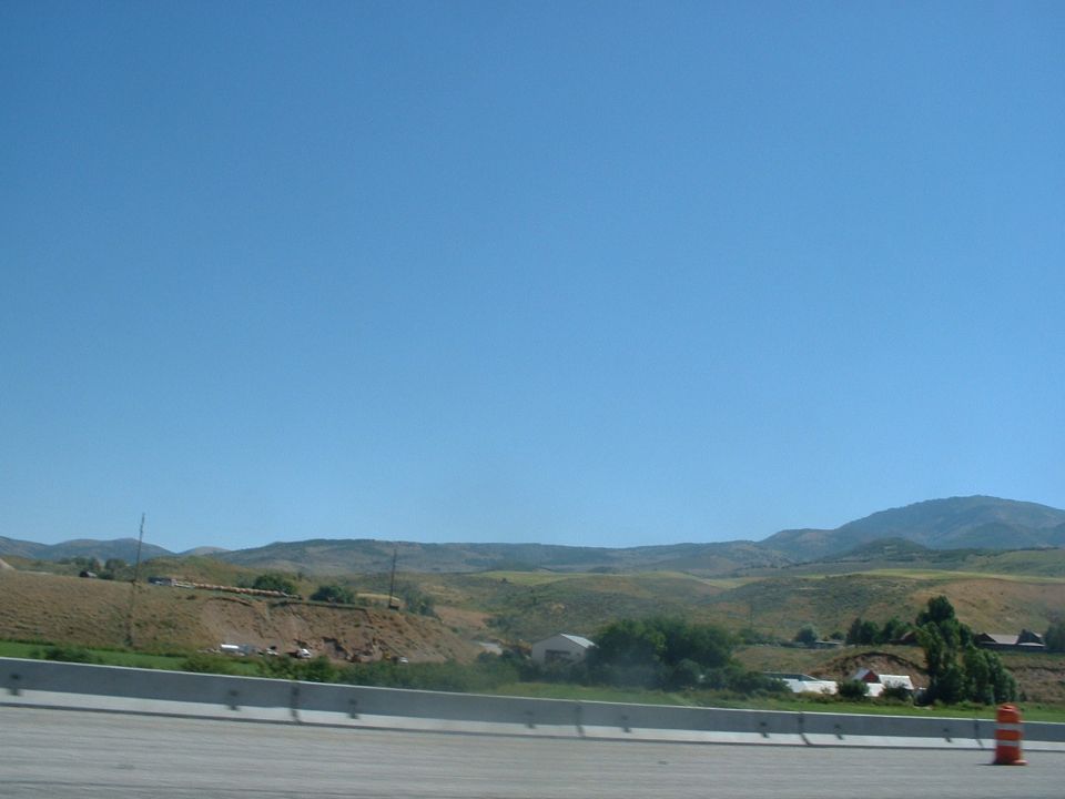 Rural landscape with rolling hills and scattered buildings under a clear blue sky