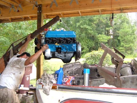 1978 Ford Bronco - A blue engine is being lowered into the engine bay of a vehicle using an engine hoist.