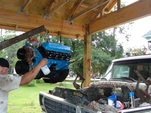 1978 Ford Bronco - Engine swap in progress: a blue V8 engine is being carefully lowered into a pickup truck.