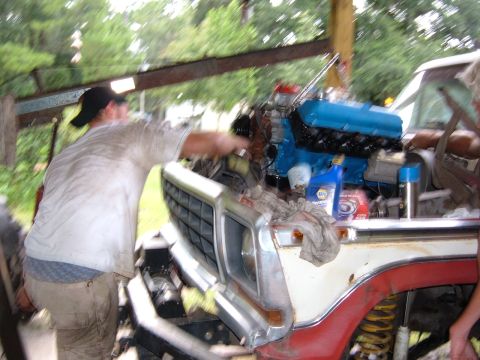 1978 Ford Bronco - Mechanic works on a blue engine installed in a Ford truck.