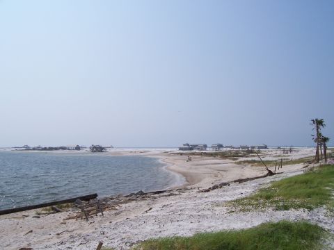 1995 Ford Bronco - A wide view of a beach with structures on stilts in the distance and the ocean on the left.