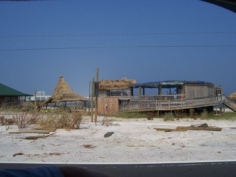 1995 Ford Bronco - Structures with thatched roofs and wooden walkways sit on a sandy beach under a clear blue sky.