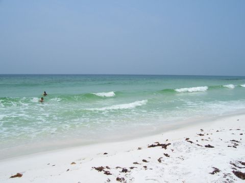 1995 Ford Bronco - A beach scene with gentle waves rolling onto the shore and two individuals enjoying a swim in the clear blue water.