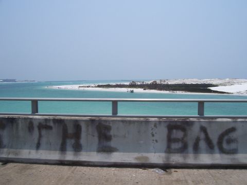 1995 Ford Bronco - Graffiti reading 'THE BAG' is spray-painted on a concrete barrier overlooking a bright blue ocean and sandy beach.