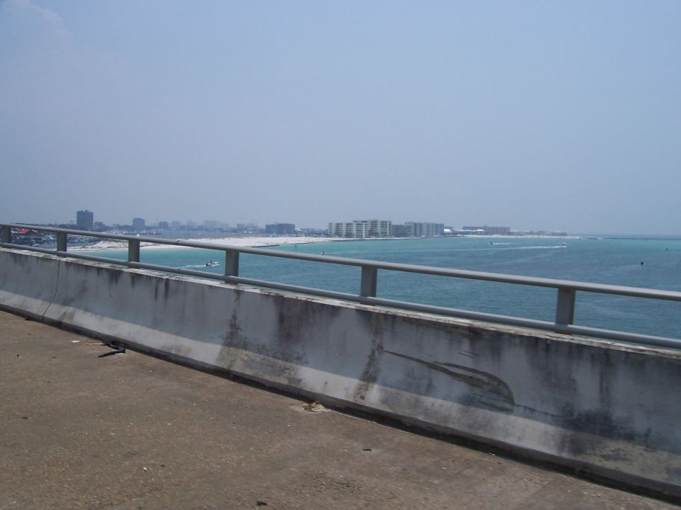 Concrete barrier on a bridge overlooking a coastline with buildings and turquoise water