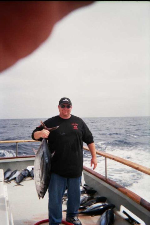 1985 Ford Bronco - A fisherman proudly displays his catch of a large tuna on a boat, with the ocean in the background.