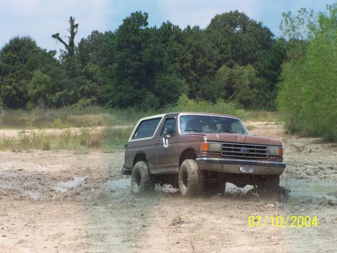 1987 Ford Bronco - A brown 1987 Ford Bronco kicks up mud as it drives through a muddy area.