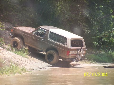 1987 Ford Bronco - 1987 Ford Bronco navigating a challenging off-road trail with water and mud.