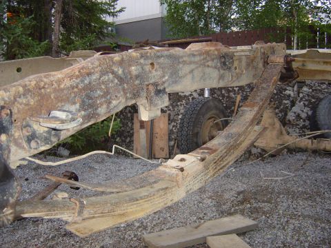 1986 Ford F-150 - The frame of a truck, showing significant rust and wear, with tires visible in the background.