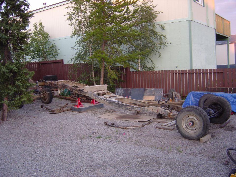 1986 Ford F-150 chassis on gravel with trees and building in background