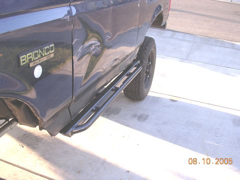1994 Ford Bronco - A dark blue Ford Bronco with aftermarket rock sliders shows extensive damage to its rear quarter panel.