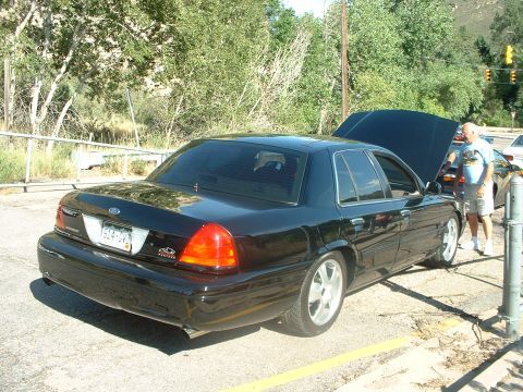 1999 Ford Crown Victoria - A black sedan, possibly a Ford Crown Victoria, is parked with its hood open, viewed from the rear quarter.
