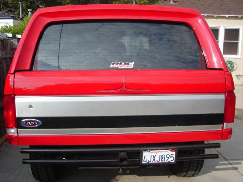 1990 Ford Bronco - rear of a red Ford Bronco SUV showing the liftgate, silver trim band, pinstripe emblem, dual-tube bumper and a California license plate rea…