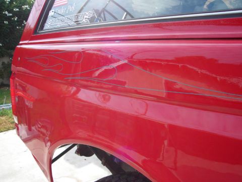 1990 Ford Bronco - Close-up of a glossy red vehicle quarter panel decorated with thin silver flame pinstriping below a window with decals.