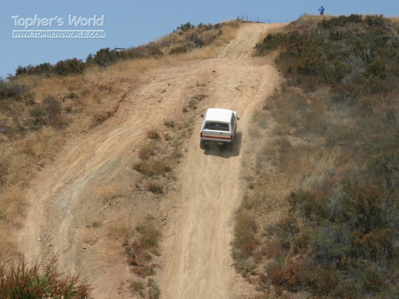 White SUV descending a steep eroded dirt hill on an off-road trail