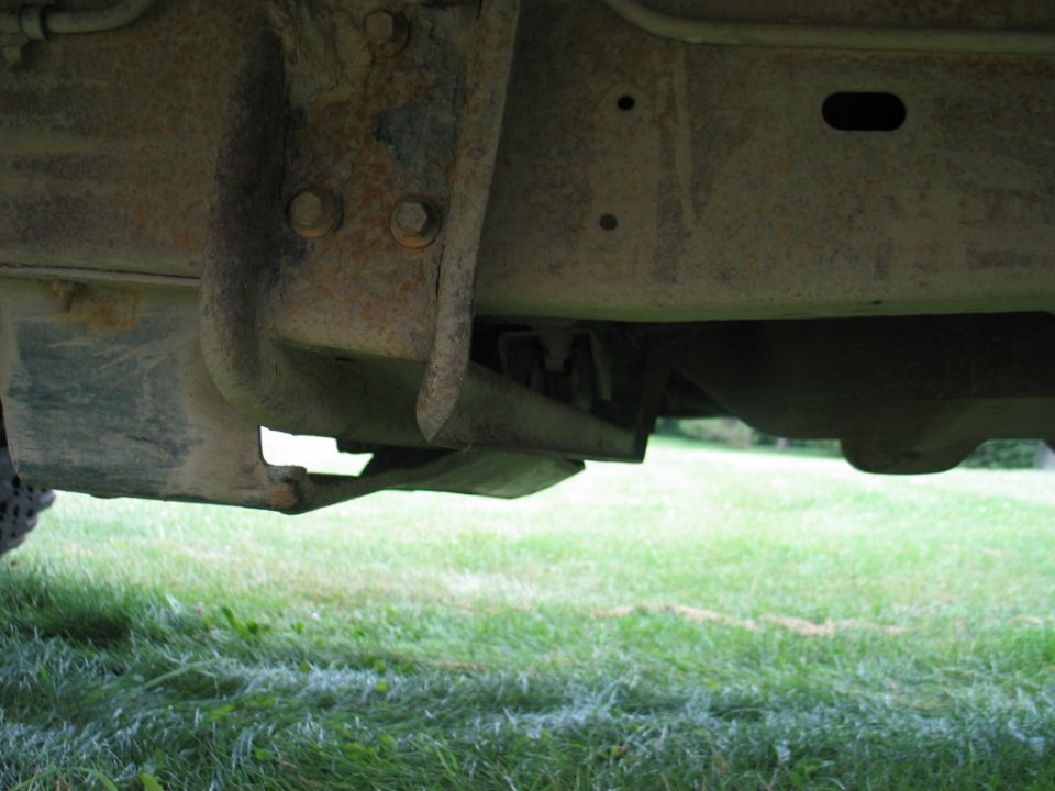 Rusty truck frame rail and bolted bracket seen from under the vehicle on grass