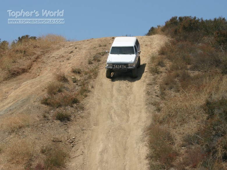 White SUV with brush guard descending a steep dirt hill against blue sky