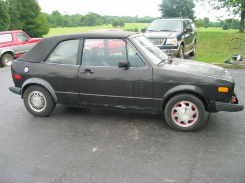 1986 Volkswagen Cabriolet - A black Volkswagen Golf Cabriolet is parked on asphalt with other vehicles and trees in the background.