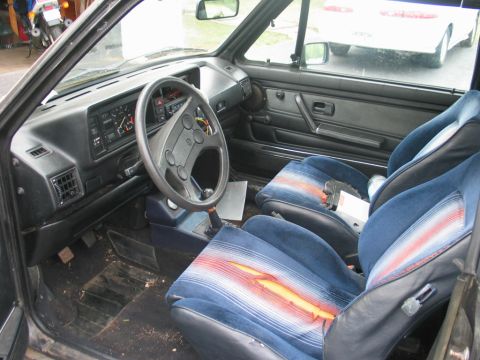 1986 Volkswagen Cabriolet - The interior of a 1986 Volkswagen Cabriolet shows blue fabric seats with red and orange stripes, and a torn driver's seat cushion.