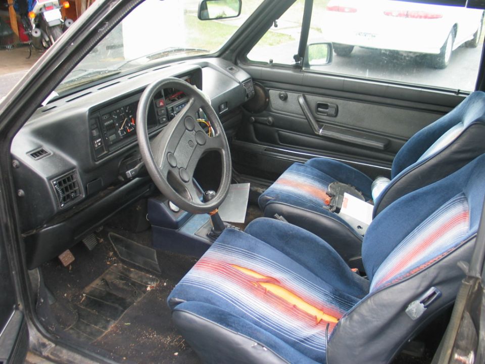 Worn VW interior with blue striped cloth seats, torn driver bolster, and black Mk1 dash