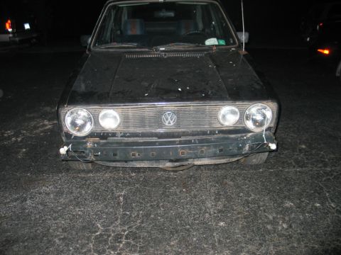 1986 Volkswagen Cabriolet - Front view of a black Volkswagen Golf Mk1, showing damage to the bumper area. Another vehicle is partially visible.