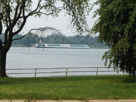 1986 Ford Bronco - A long, multi-decked boat travels down a wide river, framed by trees and a fence.