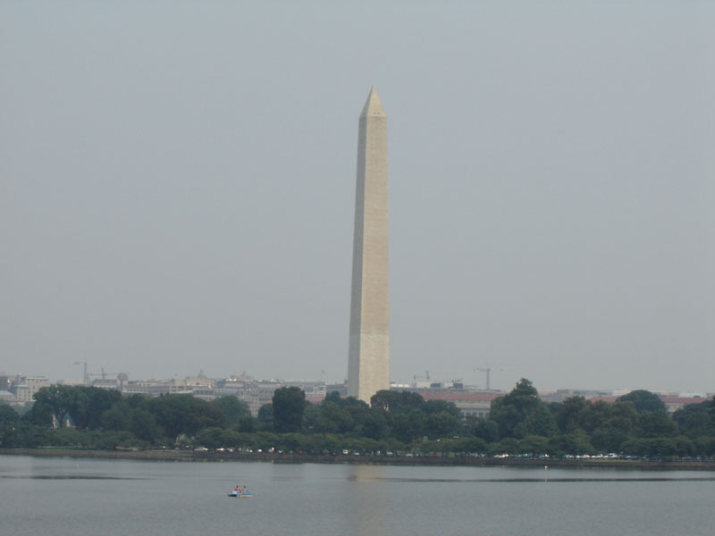 Washington Monument with a distant city skyline and a body of water in the foreground