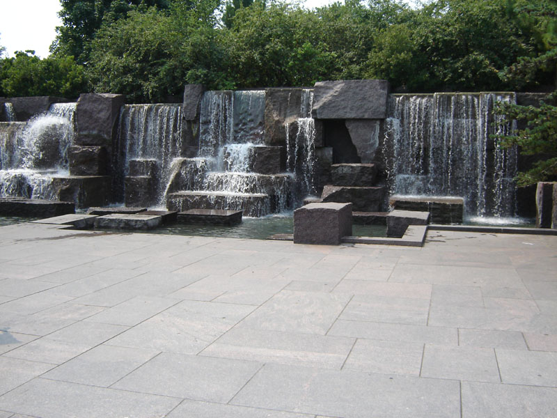 Stone plaza in front of a multi-tiered waterfall with trees in the background