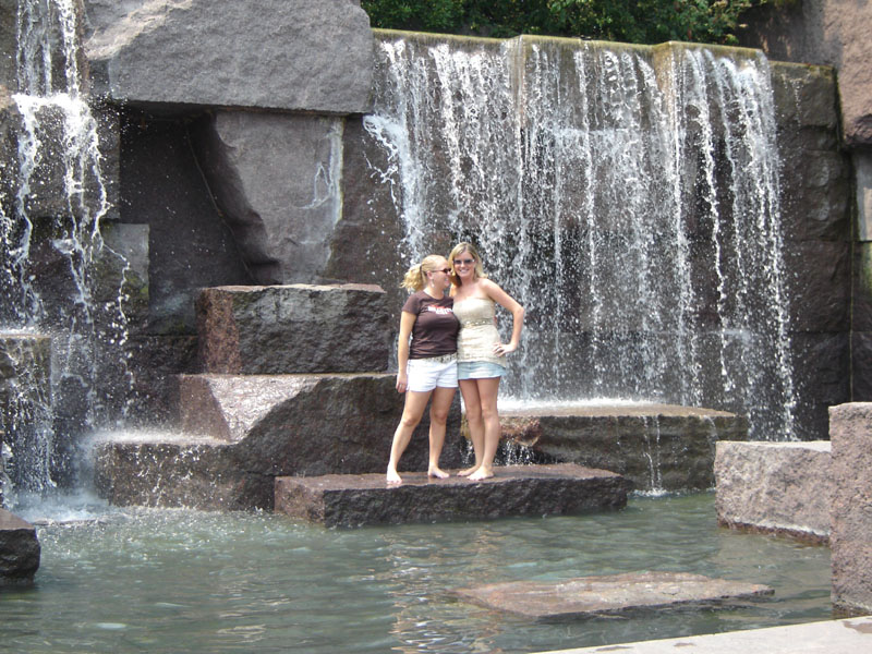 Two women stand on rocks near a cascading waterfall