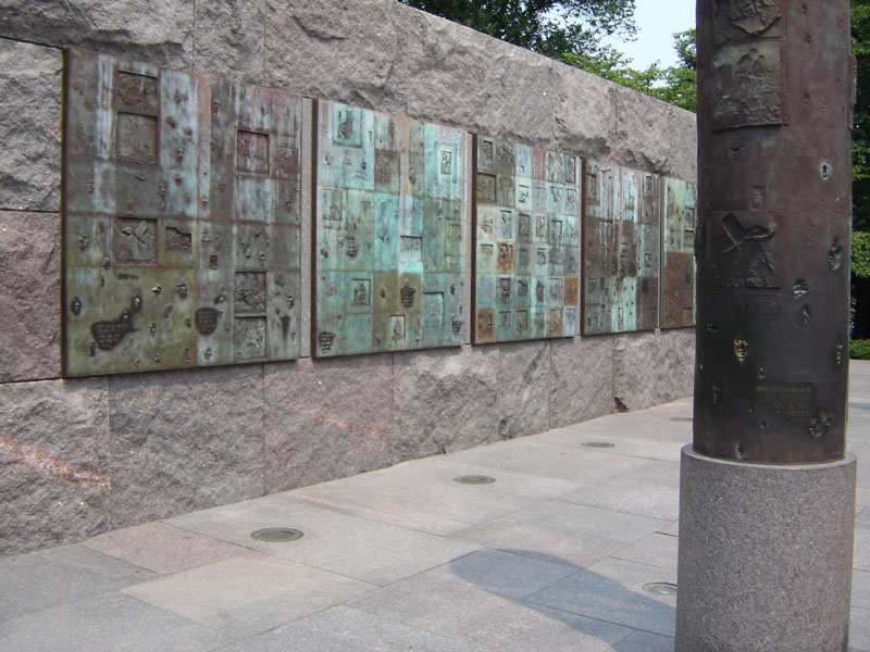 bronze relief panels on a stone wall, with a cylindrical monument to the right