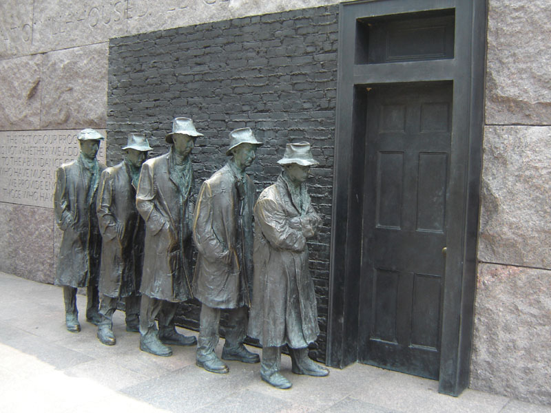 Bronze statues of men in line before a dark door, with stone and brick wall background