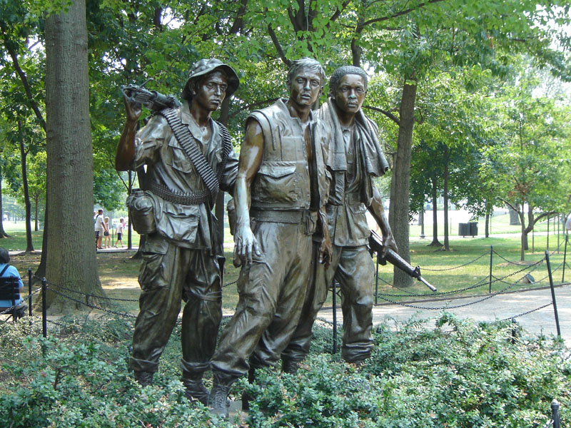 Statues of three soldiers in military uniforms, one with a machine gun, in a park setting