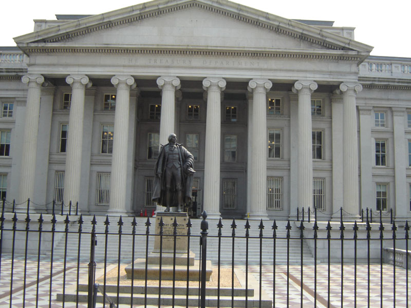Treasury Department building with columns and a statue in front, behind a black fence