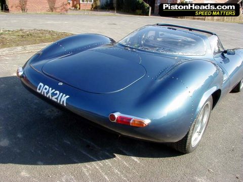 1997 Ford Crown Victoria - A blue sports car with a distinctive riveted body is seen from the rear on a paved surface.