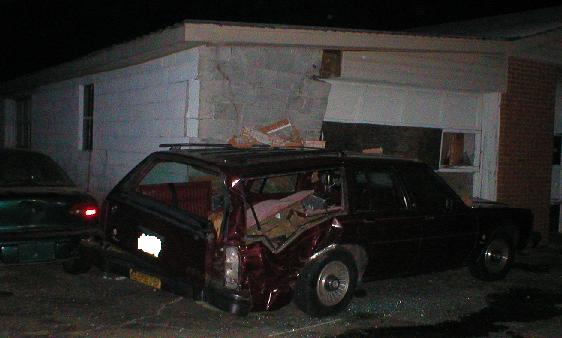 Damaged maroon station wagon, rear view, with debris in cargo area. Another dark car is visible to the left