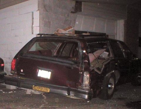 1987 Ford Crown Victoria LTD - A maroon station wagon has crashed into a building, with significant damage to the rear and side.