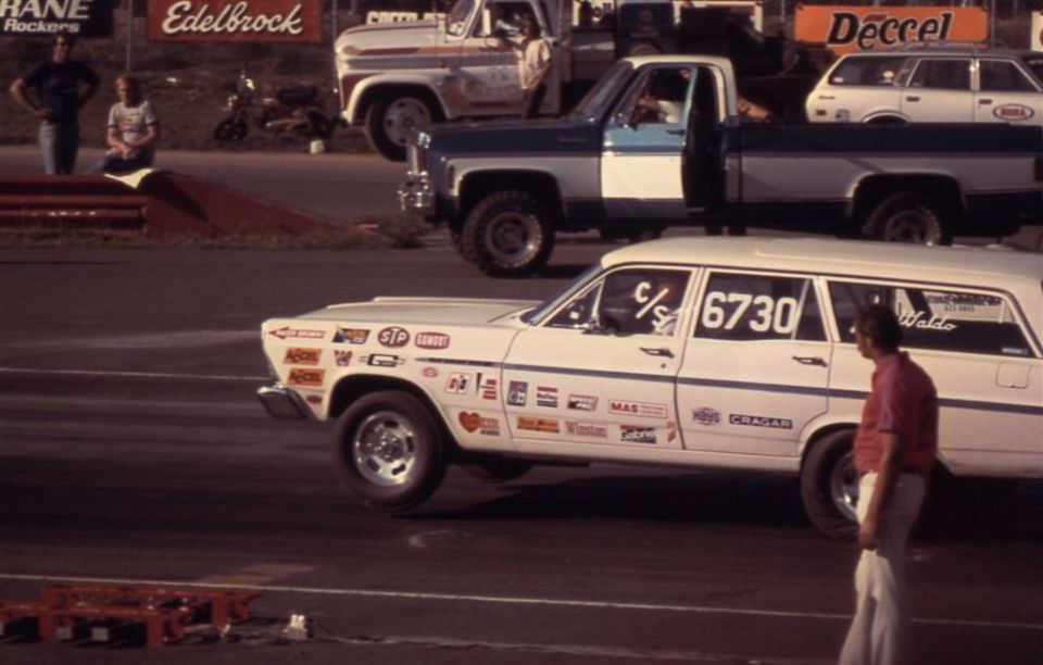 White decal-covered station wagon drag car lifting front wheels at a dragstrip