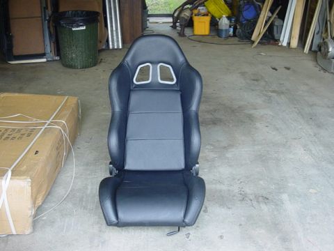 1995 Ford Mustang - A black racing car seat with silver trim is shown in a garage setting next to a cardboard box.