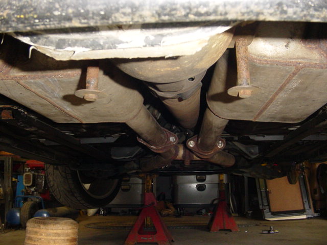 Underside view of a car's exhaust pipes and mufflers, supported by jack stands