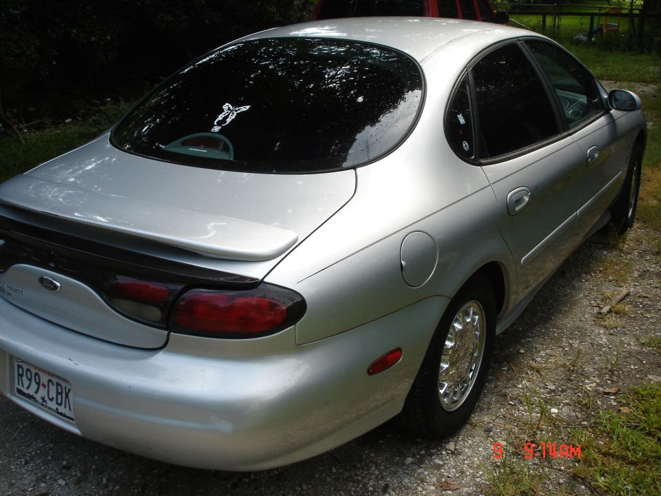 Silver Ford Taurus sedan, rear passenger-side view, parked on gravel with Missouri plate R99-CBK