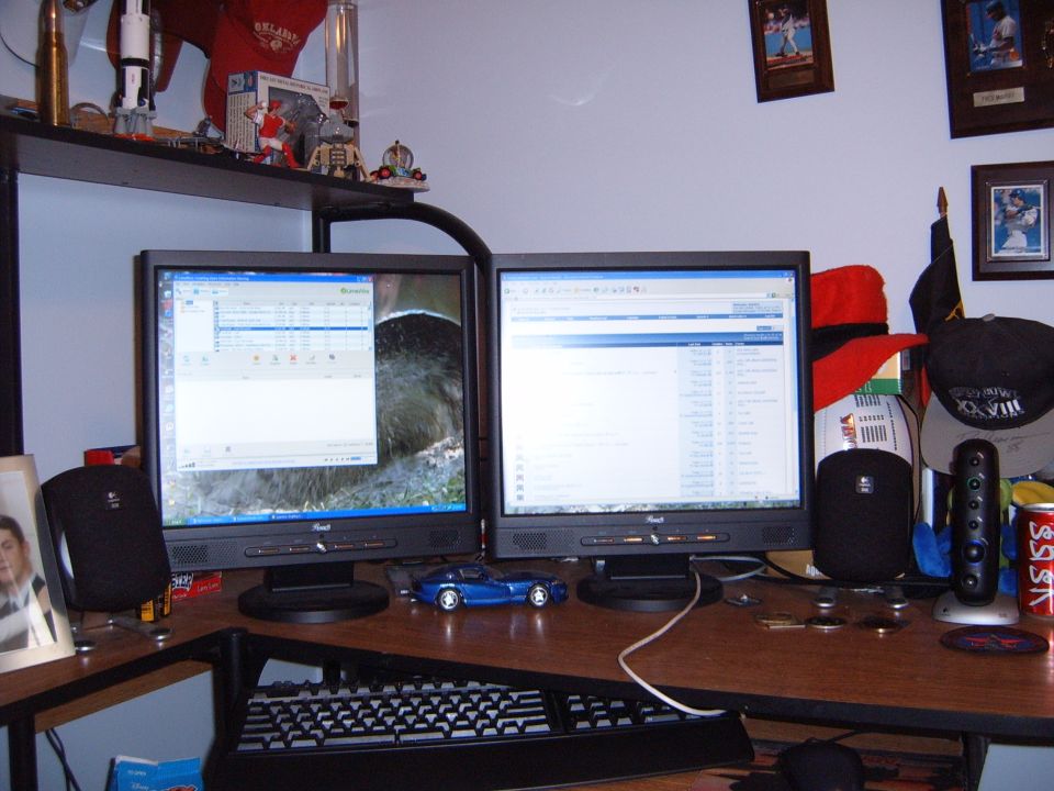 Dual computer monitors on a desk with a small blue car model, speakers, and various desk items